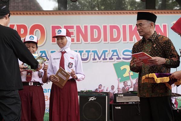 Menteri Pendidikan Muhadjir Effendy (kanan) bersiap memberikan bantuan buku cerita kepada siswa SD saat membuka Pameran Pendidikan di Purwokerto, Banyumas, Jateng (27 - 4). 