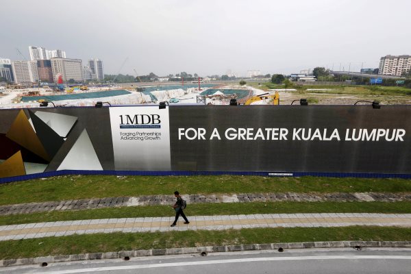 Seorang pejalan kali melintas di depan bilboard 1 Malaysia Development Berhad (1MDB) di  Kuala Lumpur (1/3/2015). - ReutersOlivia Harris