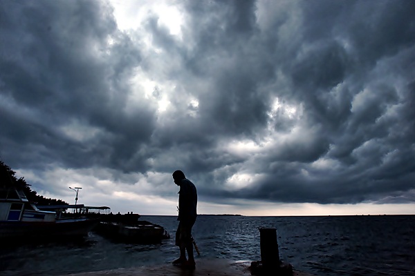 Warga beraktivitas dengan latar belakang awan hitam di Dermaga Pulau Pramuka, Kepulauan Seribu, Kamis (23/3). - Antara/Wahyu Putro A