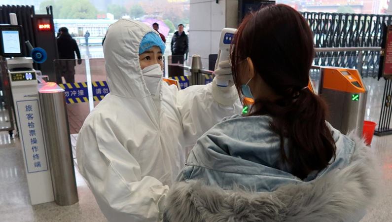 Seorang petugas berjas pelindung memeriksa suhu seorang penumpang yang tiba di Stasiun Xianning Utara, di Xianning, sebuah kota yang berbatasan dengan Wuhan di utara, di provinsi Hubei, China 24 Januari 2020. - REUTERS / Martin Pollard