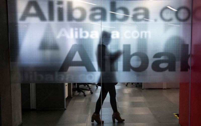 Seorang karyawan terlihat di balik dinding kaca dengan logo Alibaba di kantor pusat perusahaan itu di pinggiran Hangzhou, Provinsi Zhejiang, China. - Reuters