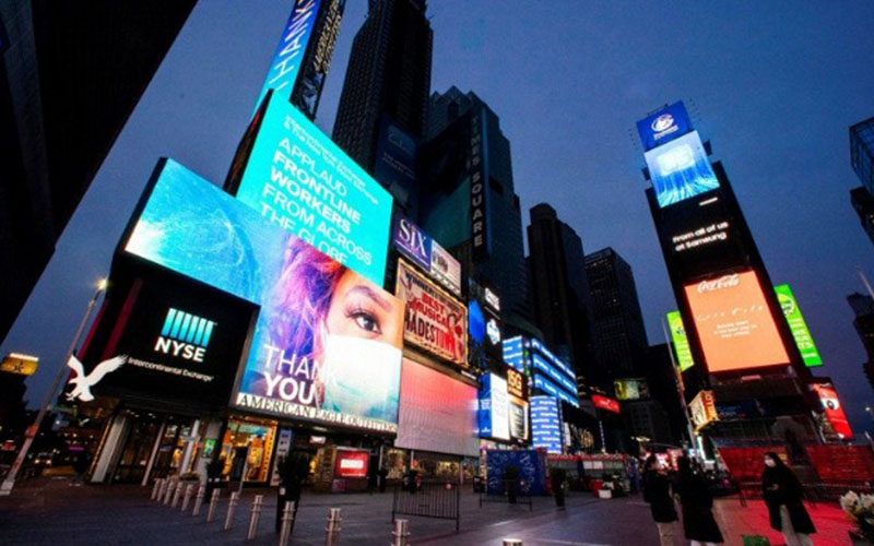 Warga berjalan di sekitar Times Square saat beberapa layar bercahaya biru sebagai bagian dari inisiatif 