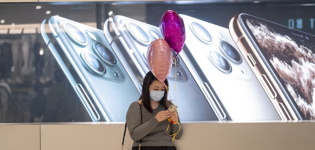Warga Hong Kong menggunakan ponselnya di depan papan iklan iPhone buatan Apple Inc. di Hong Kong, China, Jumat (14/2/2020). - Bloomberg/Justin Chin