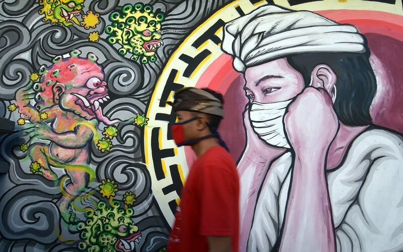 Warga melintas di dekat mural bergambar monster Covid-19 berhadapan dengan umat Hindu yang menggunakan masker di Denpasar, Bali, Senin (16/11/2020). - Antara/Nyoman Hendra Wibowo