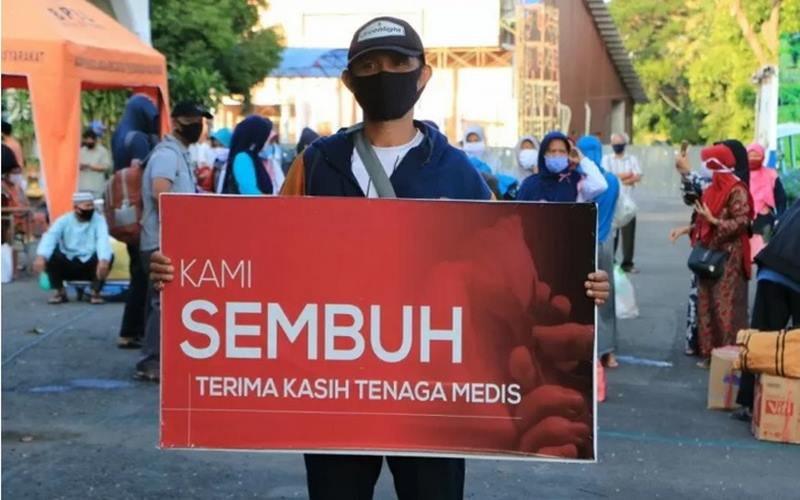 Seorang warga yang dinyatakan sembuh dari Covid-19 membawa spanduk bertuliskan ucapan terima kasih kepada tenaga medis saat dipulangkan dari tempat karantina di Asrama Haji Surabaya pekan lalu. - Antara