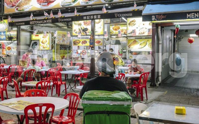 Seorang pengemudi Grab menunggu pesanan di luar restoran di Jalan Alor, Kuala Lumpur. - Bloomberg 