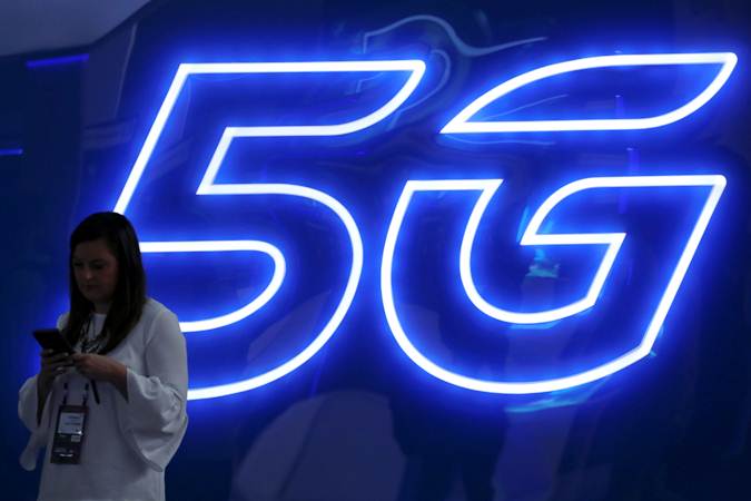 Seorang wanita mengoperasikan ponselnya di dekat logo teknologi 5G. - REUTERS/Sergio Perez