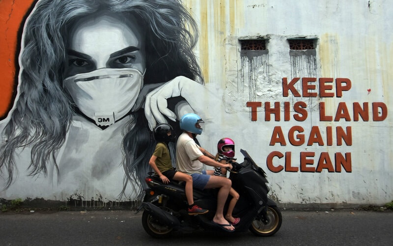 Warga negara asing melintas di dekat mural bergambar perempuan menggunakan masker di Badung, Bali, Minggu (24/1/2021). Jumlah kasus positif Covid-19 di Bali meningkat saat Pemberlakuan Pembatasan Kegiatan Masyarakat (PPKM). - Antara/Nyoman Hendra Wibowo.