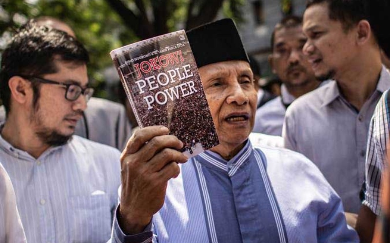 Amien Rais (tengah) menunjukkan buku berjudul Jokowi People Power saat jeda pemeriksaan untuk salat Jumat di Direktorat Reserse Kriminal Umum (Ditreskrimum) Polda Metro Jaya, Jakarta, Jumat (24/5/2019). - ANTARA FOTO/Aprillio Akbar