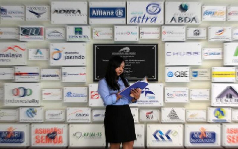 Karyawati berdiri di dekat logo beberapa perusahaan asuransi di kantor Asosiasi Asuransi Umum Indonesia di Jakarta. - Bisnis