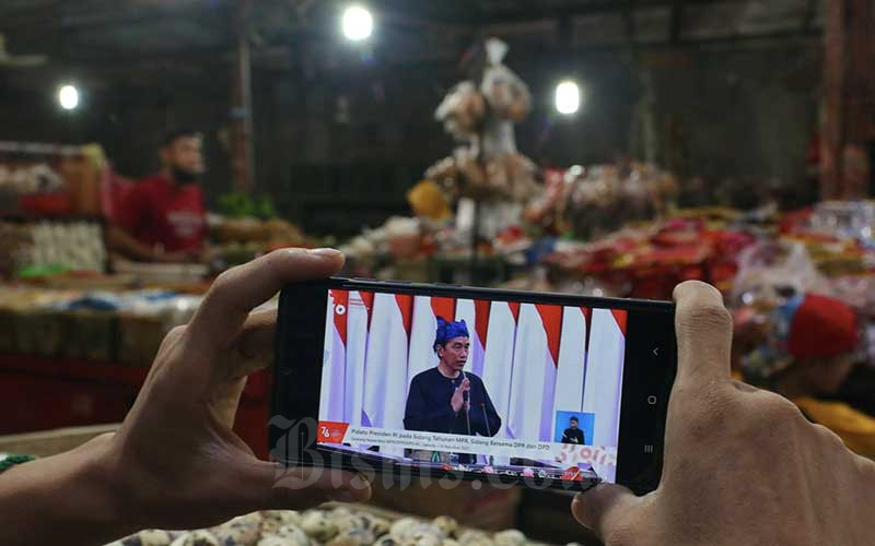 Pedagang menyaksikan Presiden Joko Widodo menyampaikan pidato dalam Sidang Tahunan MPR Tahun 2021 melalui live streaming di Jakarta, Senin (16/8/2021). Dalam kesempatan tersebut, Jokowi menyampaikan sejumlah poin penting terkait kesehatan dan penanganan pandemi Covid-19. Bisnis - Eusebio Chrysnamurti