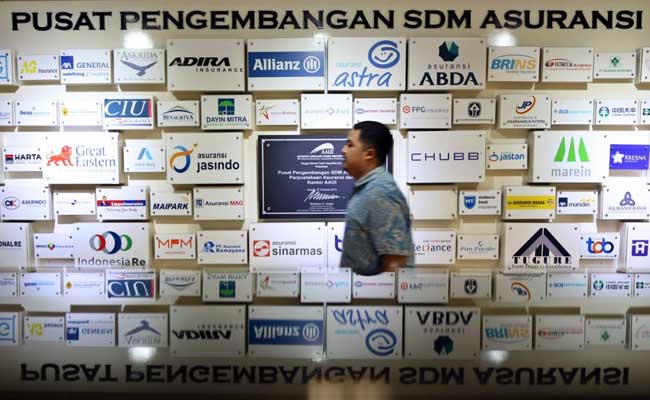 Karyawan melintasi logo-logo perusahaan asuransi di Kantor Asosiasi Asuransi Umum Indonesia (AAUI), Jakarta, Selasa (11/02/2020). Bisnis - Eusebio Chrysnamurti