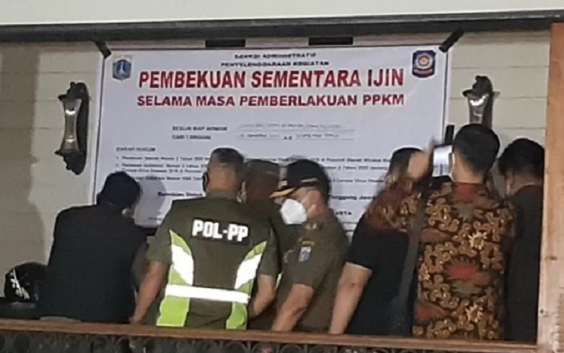 Petugas dari Satuan Polisi Pamong Praja DKI Jakarta menempelkan spanduk pembekuan sementara izin beraktivitas Holywings Kemang, Mampang Prapatan, Jakarta Selatan, Senin (6/9/2021). - Antara
