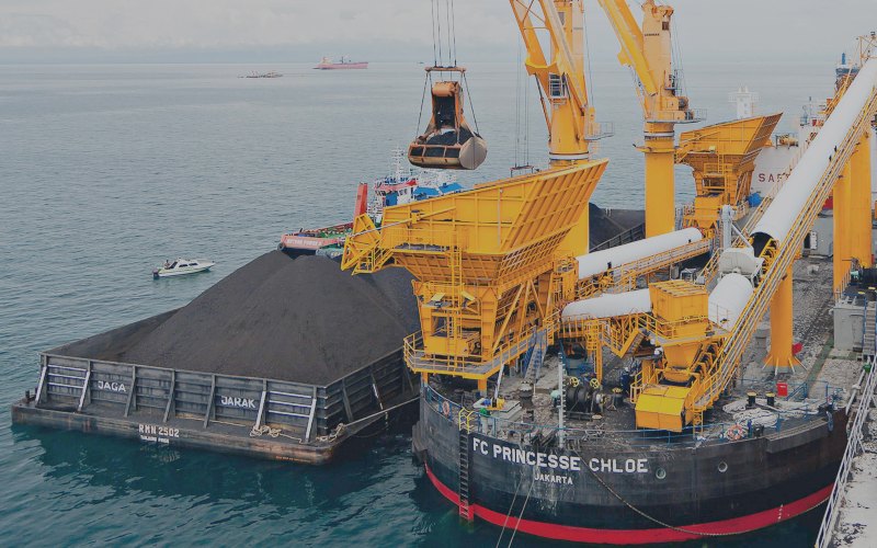 Aktivitas pemindahan muatan batu bara dari tongkang ke kapal induk dengan floating crane. - indikaenergy.co.id