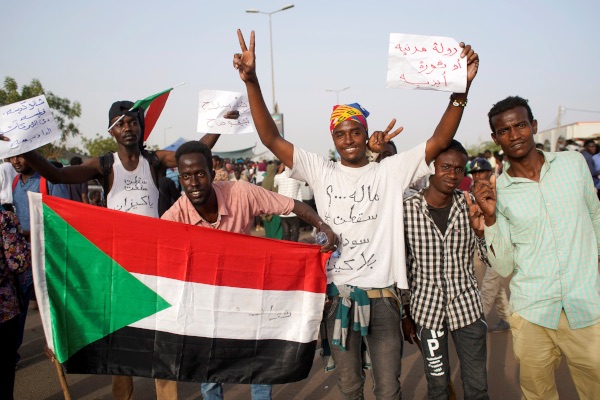 Pengunjuk rasa memegang bendera Sudan dan melantunkan slogan-slogan dalam protes terhadap pengumuman militer yang menyatakan bahwa Presiden Omar Al Bashir bakal digantikan oleh pejabat militer, di luar Kementerian Pertahanan di Khartoum, Sudan, Kamis (11/4/2019). - Reuters/Stringer