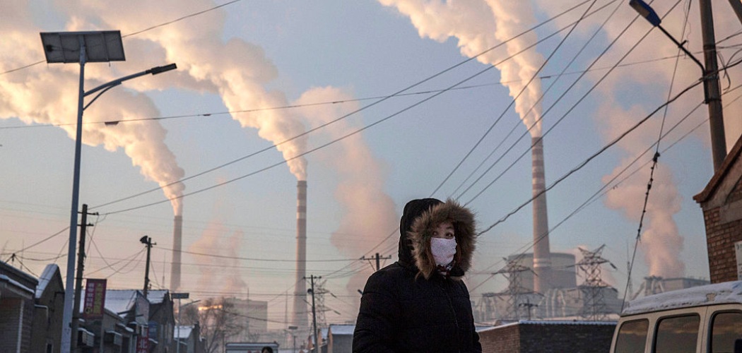 Asap mengepul saat seorang wanita mengenakan masker di dekat pembangkit listrik tenaga batu bara di Shanxi, China. Kevin Frayer / Getty Images  -  Bloomberg