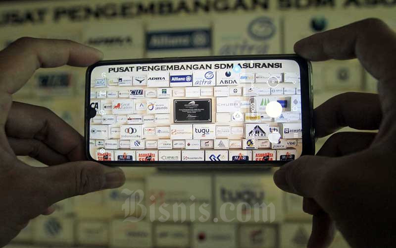 Karyawan memotret deretan logo-logo perusahaan asuransi di Kantor Asosiasi Asuransi Umum Indonesia (AAUI) di Jakarta, Selasa (22/9/2020). Bisnis - Himawan L Nugraha 