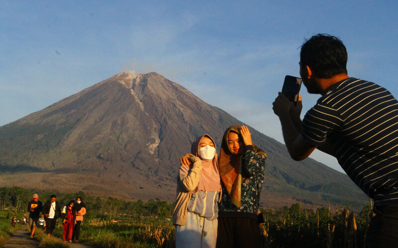 Warga berfoto dengan latar belakang gunung Semeru terlihat di desa Supiturang, Pronojiwo, Lumajang, Jawa Timur, Jumat (10/12/2021). Pusat Vulkanologi Mitigasi Bencana Geologi (PVMBG) mencatat dalam laporan per enam jam, gunung Semeru masih berada di status Waspada (level 2) dengan aktivitas awan panas serta kegempaan sebanyak tiga kali dengan amplitudo 2-6 mm dan satu kali gempa vulkanik dalam. - Antara/Ari Bowo Sucipto.