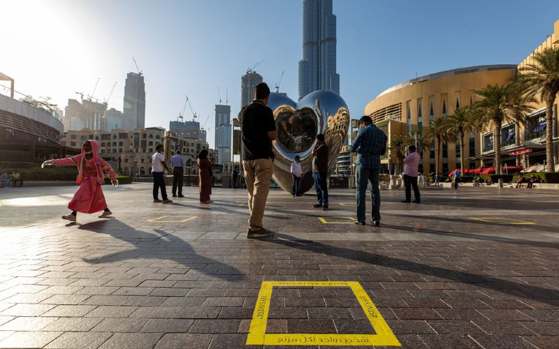 Turis berdiri di antara tanda-tanda lantai jarak sosial di dekat gedung pencakar langit Burj Khalifa di Dubai.  - Bloomberg/Christopher Pike 