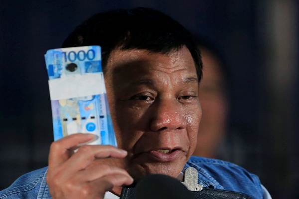  Presiden Filipina Rodrigo Duterte memegang uang peso Filipina untuk pengungsi Marawi saat berkunjung ke pusat Iligan City National School of Fisheries di Iligan City, Filipina pada tanggal 20 Juni 2017. - Reuters