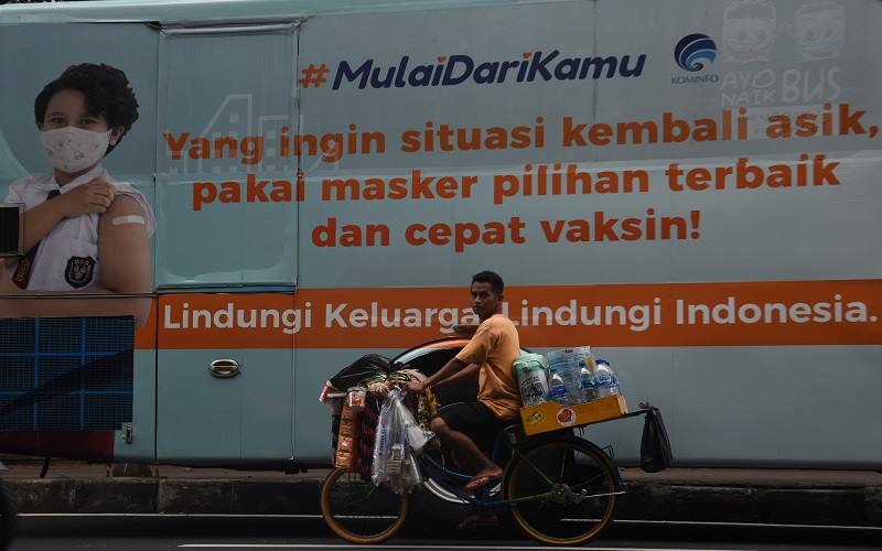 Pedagang melintas di dekat iklan layanan masyarakat tentang imbauan vaksin di kawasan Gambir, Jakarta, Senin (3/1/2022). Presiden Joko Widodo memutuskan pelaksanaan vaksinasi dosis ketiga atau 
