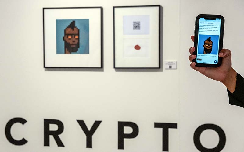 Pengunjung memegang smartphone yang menampilkan pasar online galeri di dekat NFT dan tandatangan litograf di  Gallery di London, Inggris, Rabu (22/9/2021). Bloomberg - Chris J. Ratcliffe