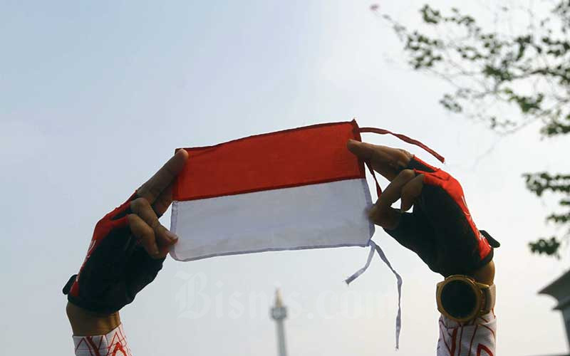 Warga menunjukan bendera merah putih mini di sekitar Monumen Nasional di Jakarta, Selasa (17/8/2021). Jelang upacara Hari Ulang Tahun Republik Indonesia ke-76, banyak warga berolahraga menggunakan atribut merah putih. Bisnis - Himawan L Nugraha