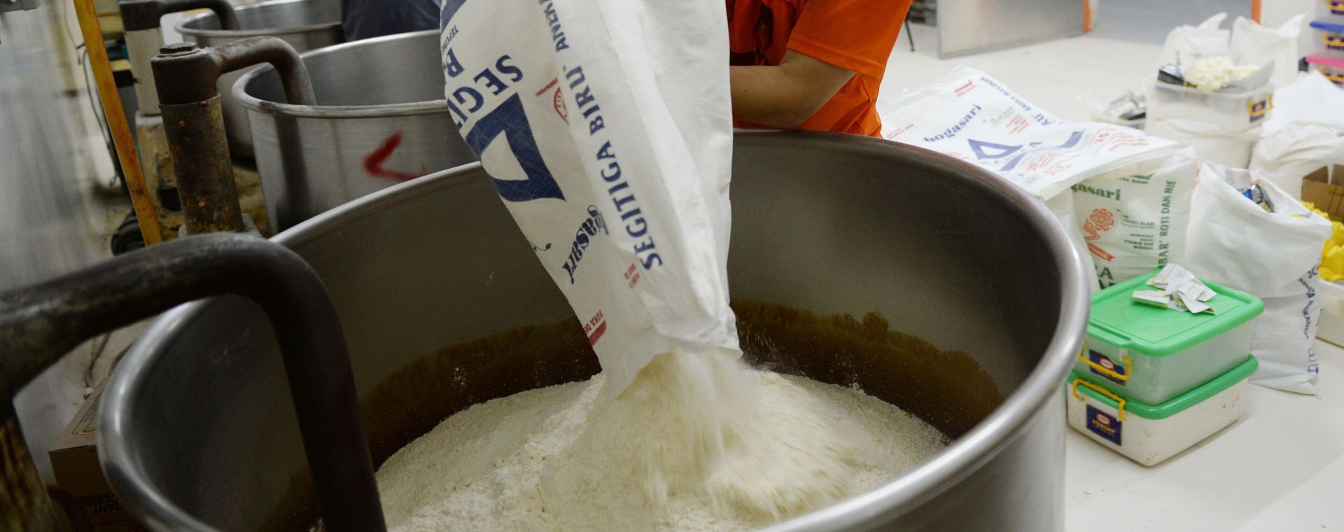Seorang karyawan menuangkan sekantong tepung terigu ke dalam mesin pencampur untuk menyiapkan adonan di pabrik roti Tan Ek Tjoan di Ciputat, Provinsi Banten, Indonesia.  - Bloomberg