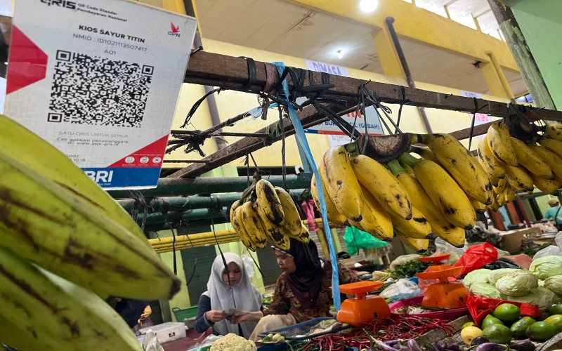 Pedagang sayur di Pasar Gubah, Titin, sedang melayani pembeli yang membayar dengan uang tunai. Kios Titin telah dilengkapi kode QRIS untuk transaksi nontunai.  - Bisnis/Dinda Wulandari
