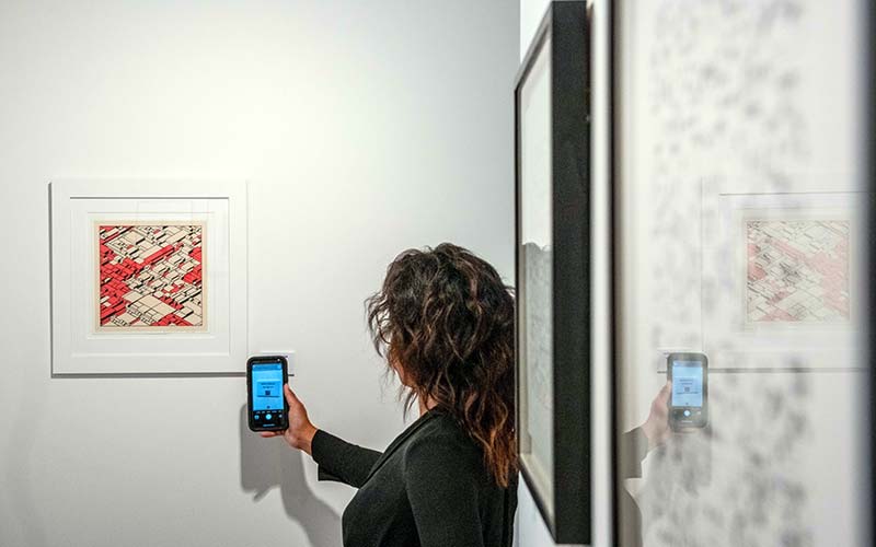 Pengunjung memegang smartphone yang menampilkan pasar online galeri di dekat NFT dan tandatangan litograf di  Gallery di London, Inggris, Rabu (22/9/2021). Bloomberg - Chris J. Ratcliffe