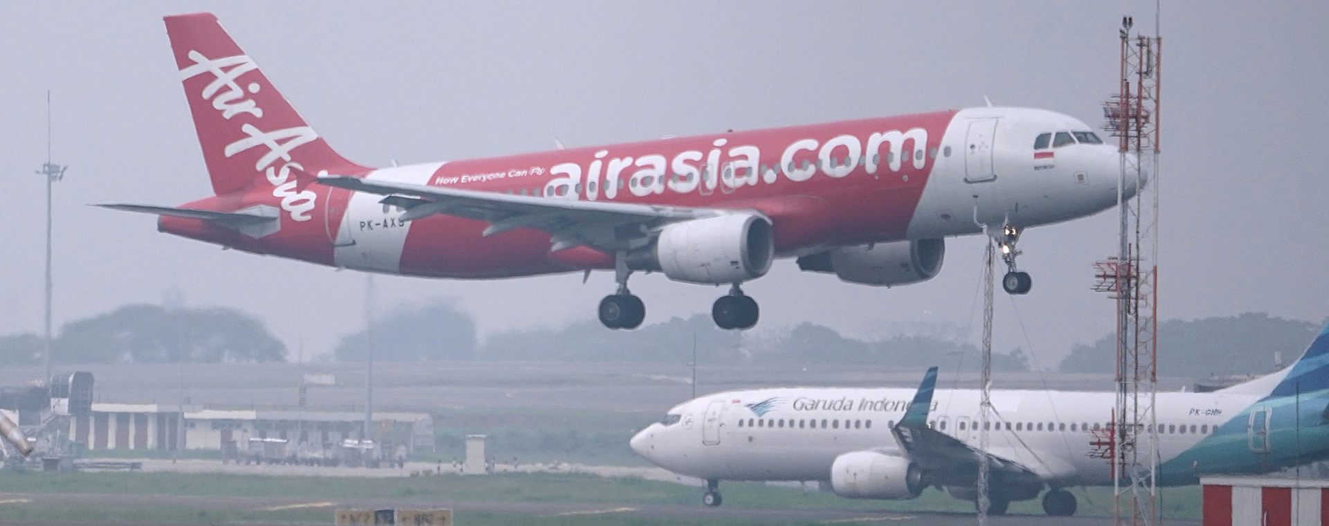 Pesawat milik PT AirAsia Indonesia Tbk. (CMPP) bersiap mendarat melewati pesawat PT Garuda Indonesia Tbk. (GIAA) di Bandara Internasional Soekarno-Hatta di Cengkareng, Senin, (24/5 - 2021). Bloomberg / Dimas Ardian