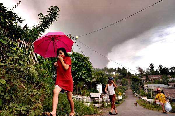 Warga berjalan di bawah hujan abu vulkanik setinggi 5.809 mdpl berwarna kelabu akibat letusan gunung Soputan, di atas Desa Kota Menara, Minahasa Selatan, Sulawesi Utara, Rabu (3/10/2018). - ANTARA/Adwit B Pramono