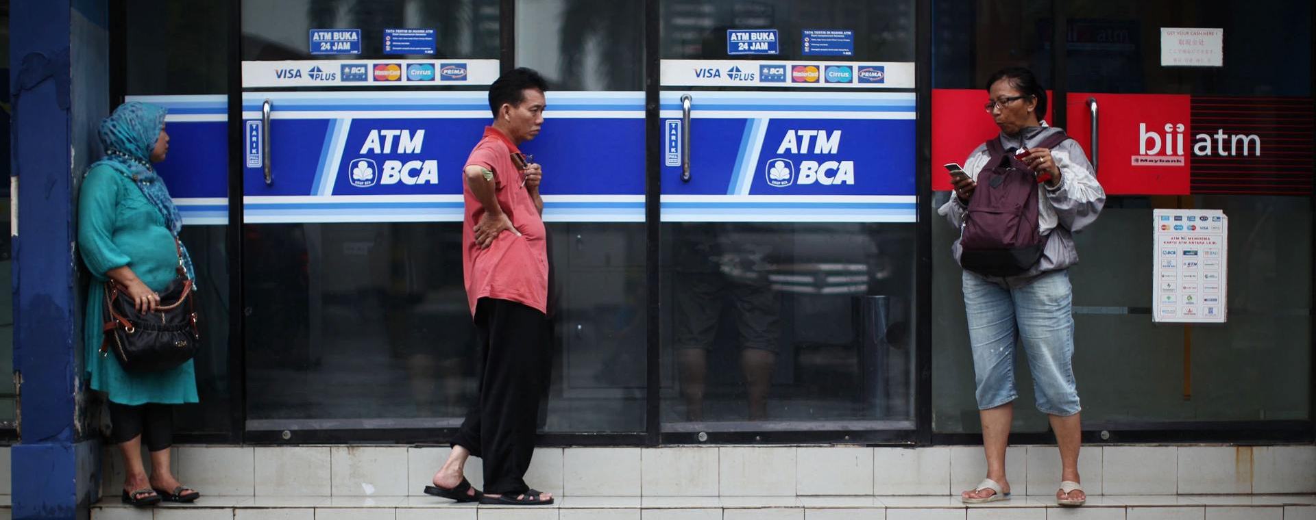 Pejalan kaki berdiri di samping fasilitas anjungan tunai mandiri (ATM) yang dioperasikan oleh PT Bank Central Asia (BCA) di Jakarta, Jumat, 18 Januari 2013. Bloomberg / Dimas Ardian