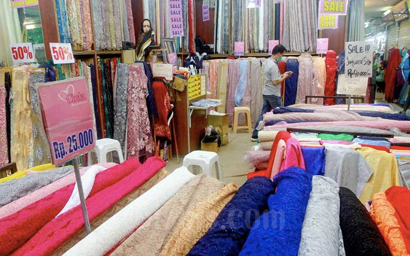 Pengunjung beraktivitas di salah satu gerai penjualan kain di Pasar Tanah Abang, Jakarta, Minggu (5/12/2021). Asosiasi Serat dan Benang Filament Indonesia (APSyFI) memproyeksikan kenaikan tarif dasar listrik (TDL) akan menurunkan utilisasi industri tekstil hingga 10 persen. Dari sisi industri, pengusaha akan langsung mengalihkan beban kenaikan harga pokok produksi (HPP) ke konsumen. Bisnis/Himawan L Nugraha