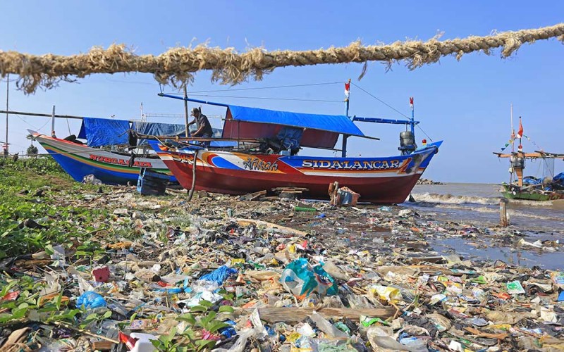 Nelayan memperbaiki perahu di sekitar pantai yang dipenuhi sampah plastik di Juntinyuat, Indramayu, Jawa Barat, Rabu (22/6/2022). Pemerintah Indonesia berkomitmen untuk mengurangi sampah plastik di laut dengan diterbitkannya Rencana Aksi Nasional Penanganan Sampah Plastik Laut dan menargetkan pengurangan sebesar 70 persen di tahun 2025. ANTARA FOTO/Dedhez Anggara