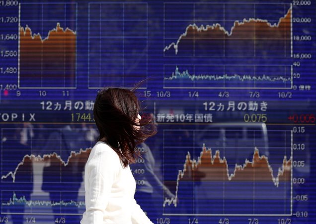 Seorang wanita berjalan melewati papan elektronik yang menunjukkan grafik pergerakan indeks Nikkei Jepang baru-baru ini. - Reuters