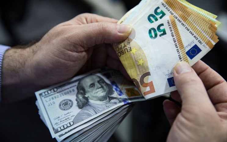 Seorang pria menghitung lembaran uang euro dan dolar AS. - Bloomberg/Kerem Uzel