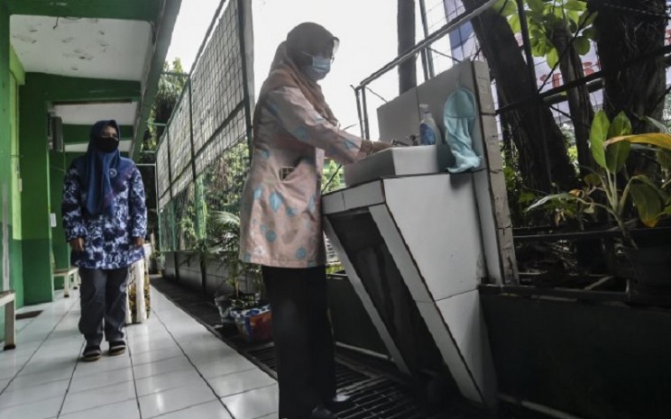 Orangtua murid mencuci tangan sebelum masuk ke dalam kelas saat mengikuti simulasi sekolah campuran tatap muka dan daring (hybrid) di SMP 255, Jakarta Timur, Selasa (30/3/2021). - Antara