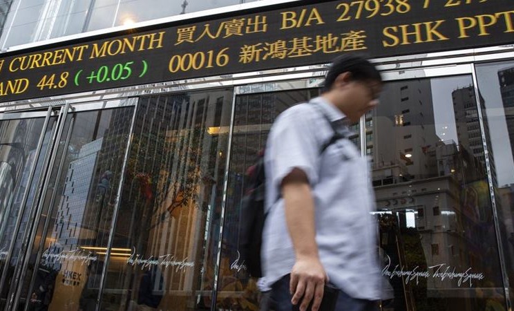 Seorang pejalan kaki berjalan melewati papan ticker elektronik yang menampilkan angka harga saham di luar kompleks Exchange Square di Hong Kong. -  Justin Chin / Bloomberg