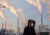 Asap mengepul saat seorang wanita mengenakan masker di dekat pembangkit listrik tenaga batu bara di Shanxi, China. Kevin Frayer / Getty Images / Bloomberg