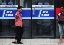 Pejalan kaki berdiri di samping fasilitas anjungan tunai mandiri (ATM) yang dioperasikan oleh PT Bank Central Asia (BCA) di Jakarta, Jumat, 18 Januari 2013. Bloomberg - Dimas Ardian